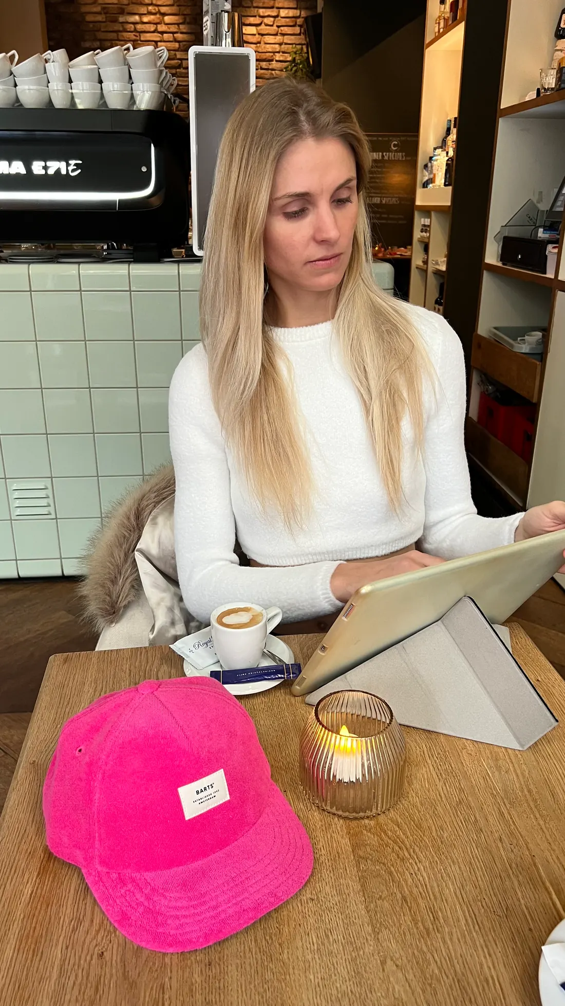 Anaïs à une table de café, tablette et casquette posées